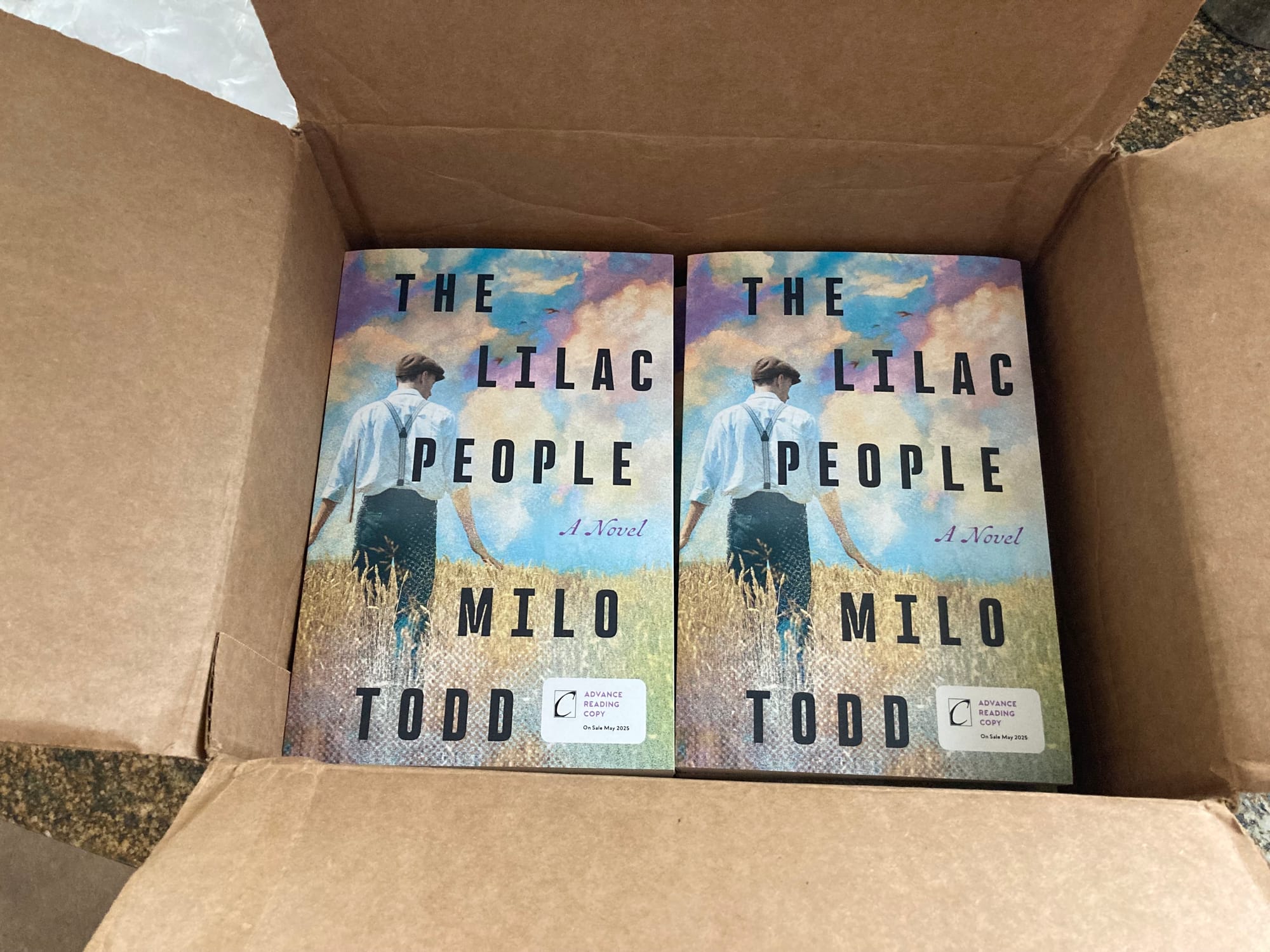 A cardboard box with its flaps open shows the two top copies of the book packed side by side.